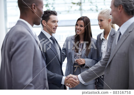 Climbing up the corporate ladder. A diverse group of businesspeople looking on as a coworker and their boss shake hands. 88316758