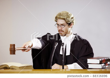 Silence. Serious young judge sitting in the courtroom with a stern facial expression while holding out a gavel. 88316896