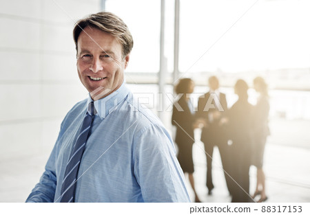 Im all about business. Cropped portrait of a businessman standing a lobby with his colleagues in the background. Im all about business. Cropped portrait of a businessman standing a lobby with his colleagues in the background. 88317153
