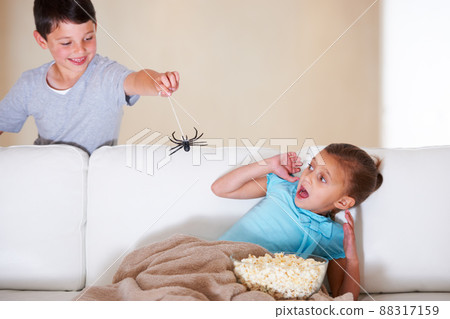 Gotcha. Mischievous young boy scaring his little sister at Halloween with a rubber spider. 88317159