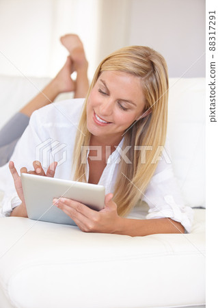 Going online in comfort. A beautiful young blonde woman working on her digital touchpad. Going online in comfort. A beautiful young blonde woman working on her digital touchpad. 88317291