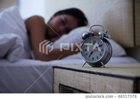 Sleeping the day away. A young woman sleeping with her alarm clock next to her bed. 88317378