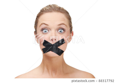 Silenced by the system. A young blonde woman looking shocked with duct tape covering her mouth. 88317792