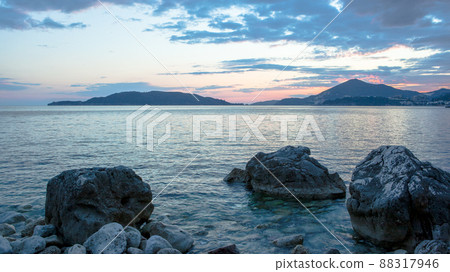Blue seascape with stoney beach at sunset. Stone coastline with islands on the skyline for publication, poster, calendar, post, screensaver, wallpaper, postcard, banner, cover, website, space for your 88317946