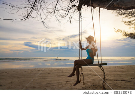 Silhouette woman wear swimsuit and straw hat swing the swings at the beach on summer vacation at sunset. 88328078