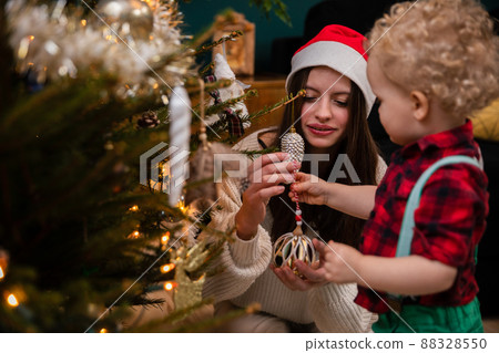 A sister helps her young brother hang ornaments for the Christmas tree. 88328550