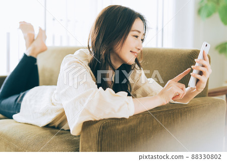 一個女人躺在沙發上，看著她的智能手機 88330802