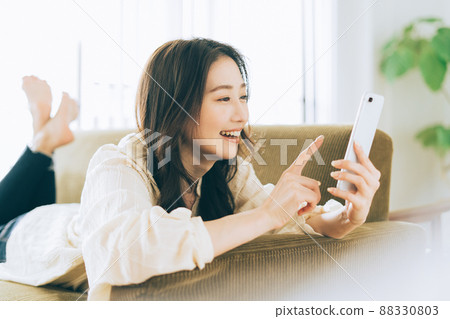 一個女人躺在沙發上,看著她的智能手機 一個女人躺在沙發上,看著她的智能手機 88330803