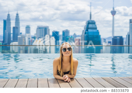 Young woman in outdoor swimming pool with city view in blue sky 88333870