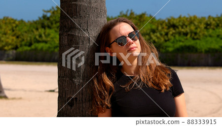 Young woman leaning against a palm tree at Miami Beach 88333915