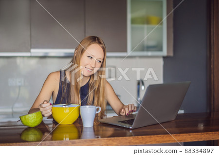 Beautiful woman having coffee and fruits for breakfast and looks into the laptop 88334897