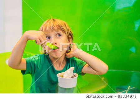 Happy young boy eating a tasty ice cream or frozen yogurt Happy young boy eating a tasty ice cream or frozen yogurt 88334972