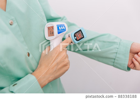 Temperature measurement gun in doctor hands. Close-up shot of doctor wearing protective surgical mask ready to use infrared isometric thermometer gun to check body temperature for virus symptoms. 88338188