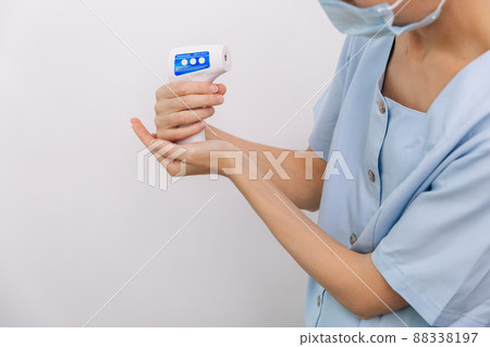 Temperature measurement gun in doctor hands. Close-up shot of doctor wearing protective surgical mask ready to use infrared isometric thermometer gun to check body temperature for virus symptoms. Temperature measurement gun in doctor hands. Close-up shot of doctor wearing protective surgical mask ready to use infrared isometric thermometer gun to check body temperature for virus symptoms. 88338197
