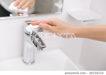 Cleaning the sink faucet with a microfiber cloth. Sanitize surfaces prevention in hospital and public spaces against corona virus. Woman hand using wet wipe. Cleaning the bathroom. 88338210