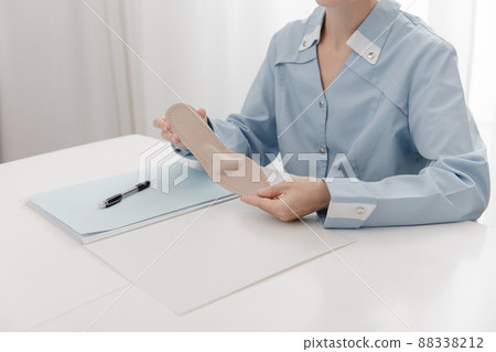 Doctor holding an insole while sitting at a table. Orthopedist tests the medical device. Orthopedic insoles. Foot care. Flat Feet Correction. Treatment and prevention of flat feet and foot diseases. Doctor holding an insole while sitting at a table. Orthopedist tests the medical device. Orthopedic insoles. Foot care. Flat Feet Correction. Treatment and prevention of flat feet and foot diseases. 88338212