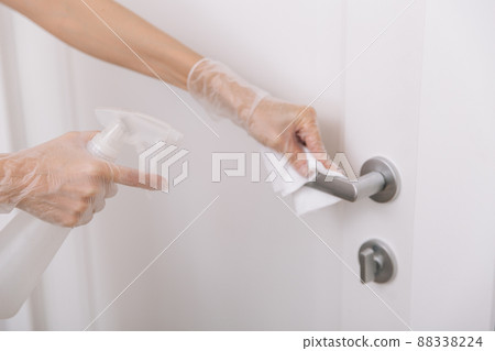 Cleaning door handles with wet wipe and white gloves. Sanitize surfaces prevention in hospital and public spaces against corona virus. Woman hand using towel for cleaning home room door link. 88338224