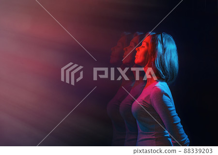 The concept of psychology and perception. The woman stands in profile, eyes closed, against a black background. Blue and red light. Copy space 88339203