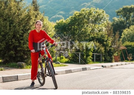 Sports lifestyle and Cycling. A young beautiful smiling woman in sportswear rides a Bicycle. In the background, the road and mountains, a Sunny day. Copy space 88339835