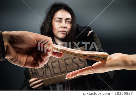 Man gives a stack of cash to woman, hands close up. Defocused disheveled woman holds a cardboard sign with the text homeless on the background. The concept of helping the homeless and vagrants Man gives a stack of cash to woman, hands close up. Defocused disheveled woman holds a cardboard sign with the text homeless on the background. The concept of helping the homeless and vagrants 88339887