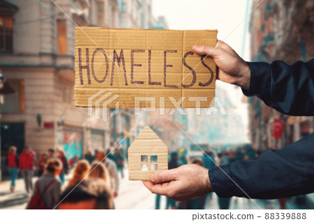 A man hold a cardboard house and sign with the inscription HOMELESS. Defocused background with street and people. Hands close-up. The concept of helping vagabonds 88339888