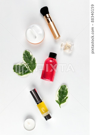 Cosmetics and self-care. A composition of green leaves, cream, brush, shower gel, perfume, oil in a tube and a candle are laid out on a white background. Flat lay. Vertical 88340159