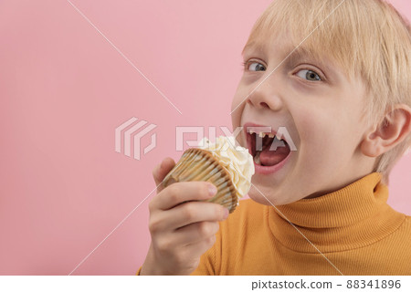 Portrait close up boy wants to eat cupcake. Blond child with muffin in his hands on pink background. Copy space 88341896