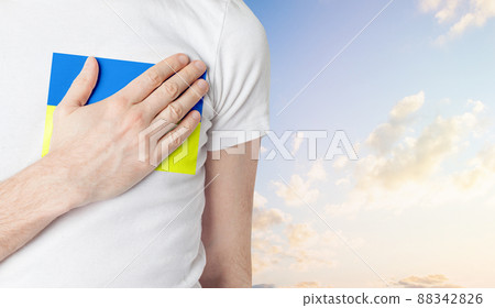 Man holding his hand near his heart with flag of Ukraine against sky clouds background. 88342826