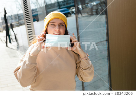 Happy smiling Woman taking off mask outdoor. Coronavirus ended. We are safe. Cheerful young woman in yellow hat removing protective mask off her face. Happy smiling Woman taking off mask outdoor. Coronavirus ended. We are safe. Cheerful young woman in yellow hat removing protective mask off her face. 88343206