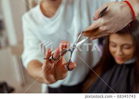 Hairdresser holding scissors in his hands and cutting client hair Hairdresser holding scissors in his hands and cutting client hair 88345743