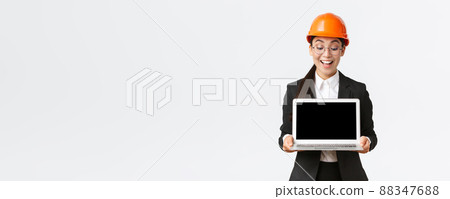 Impressed happy asian female chief engineer showing great results of enterprise to investors, standing in safety helmet and business suit, holding laptop and look pleased at computer screen Impressed happy asian female chief engineer showing great results of enterprise to investors, standing in safety helmet and business suit, holding laptop and look pleased at computer screen 88347688