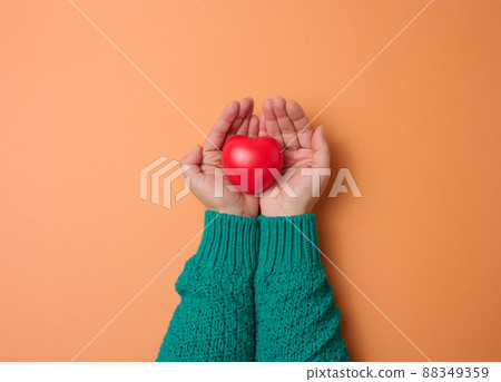 female hands holds red heart, orange background. Love and donation concept female hands holds red heart, orange background. Love and donation concept 88349359
