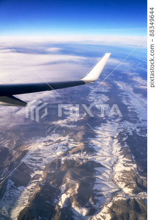 Flying and traveling. View from airplane window on the wing during sunset. Plane over mountains in winter. 88349644