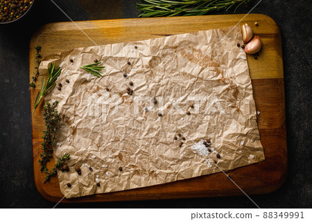 Wooden cutting board with sea salt, pepper and herbs covered with craft paper. Top view on black stone table with copy space 88349991
