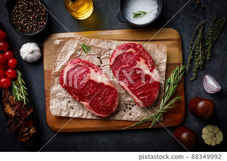 Raw pork steak pieces with spices and herbs rosemary, thyme, basil, salt and pepper on rustic wooden cutting board. Flat lay over dark black stone background 88349992