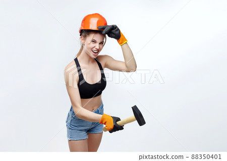 attractive blonde in an orange protective helmet makes a swing with a hammer. attractive blonde in an orange protective helmet makes a swing with a hammer. 88350401