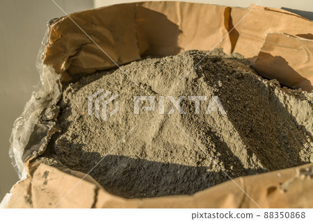 Grey sand-concrete dry mix in an open paper bag. Concrete dry powder for leveling walls and floors. Repair in the house with your own hands. DIY. Selective focus Grey sand-concrete dry mix in an open paper bag. Concrete dry powder for leveling walls and floors. Repair in the house with your own hands. DIY. Selective focus 88350868