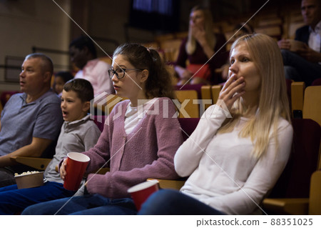 Spectators eating popcorn and watching horror movie in cinema Spectators eating popcorn and watching horror movie in cinema 88351025