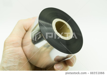 Single thermal transfer ribbon in hand. Wax thermo ribbon on cardboard reel for barcode. Supply material for printing industry. Selective focus, isolated on white Single thermal transfer ribbon in hand. Wax thermo ribbon on cardboard reel for barcode. Supply material for printing industry. Selective focus, isolated on white 88351066