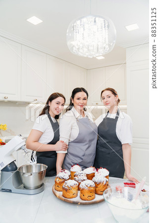 mother and daughters with Kraffins, easter cakes and Panettones in the kitchen. mother and daughters with Kraffins, easter cakes and Panettones in the kitchen. 88351125