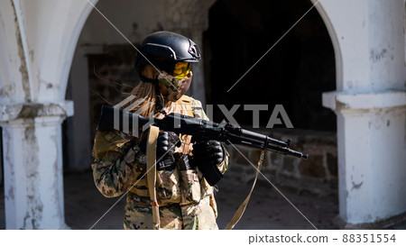 Caucasian woman in a protective suit with a machine gun. A female soldier in a camouflage uniform holds a weapon. Caucasian woman in a protective suit with a machine gun. A female soldier in a camouflage uniform holds a weapon. 88351554