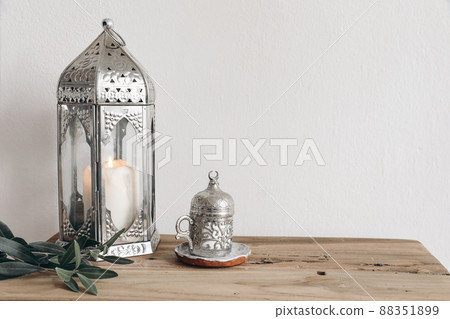 Ramadan Kareem, iftar dinner still life. Ornamental silver lantern with candle and cup with Turkish tea or coffee. Green olive tree branches on vintage wooden table background. Muslim design, Eid Adha 88351899