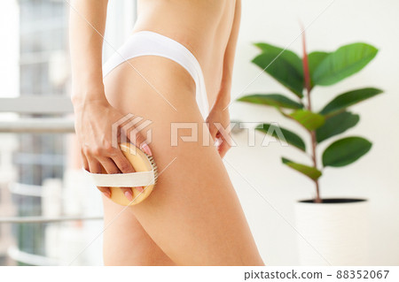 Woman holding wooden brush and doing dry massage on her feet 88352067