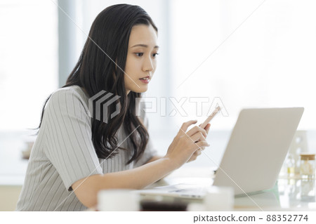 A woman who operates a smartphone while watching a computer 88352774