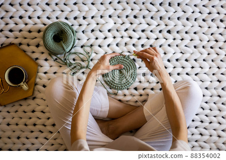 Top view creative woman knitting use ribbon yarn and crochet needle sitting on warm white plaid 88354002