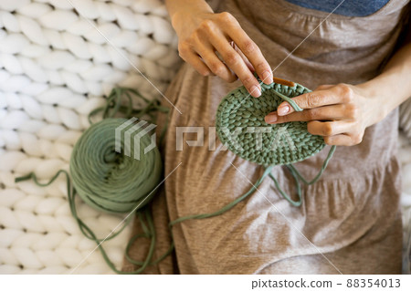 Closeup female hands knitting interior decor basket use green ribbon yarn and crochet needle Closeup female hands knitting interior decor basket use green ribbon yarn and crochet needle 88354013