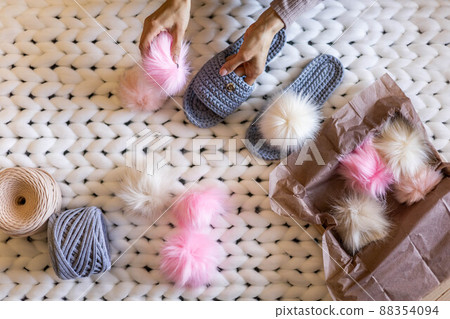 Woman hands connected fluffy fur pom pom to handmade ribbon yarn knitted slippers before sending 88354094
