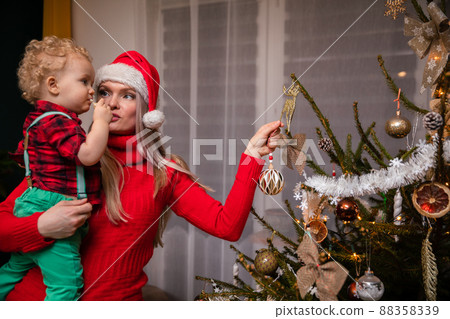 Mom asks her two-year-old son where to hang the ornament on the Christmas tree. 88358339