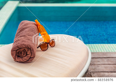 Suntan vacation hotel swimming pool background with travel accessories to tan on sun loungers holidays in Caribbean destination. Tanning oil, towel and sunglasses women objects 88358976