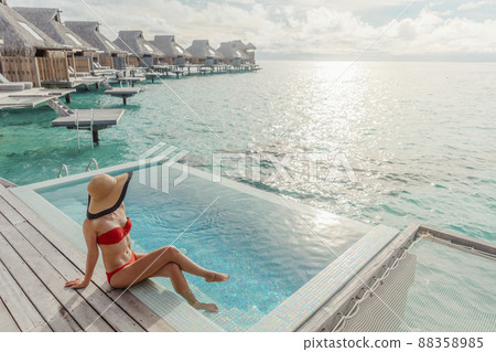 Luxury travel vacation in Bora Bora high end resort hotel tourist lady tanning in bikini by the swimming pool at overwater villa suite 88358985